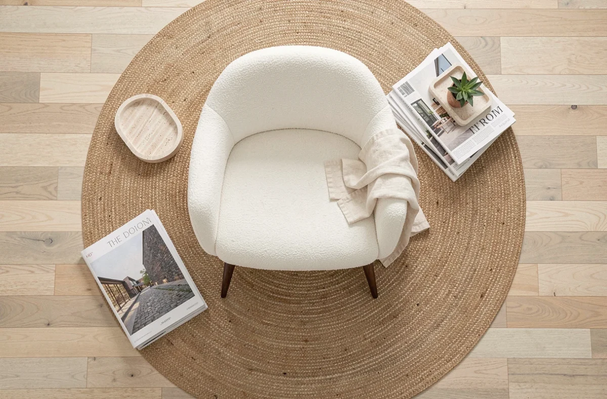 Vue aérienne d'un fauteuil design coque blanche en bouclé sur tapis jute rond entouré d'objets décoratifs et magazines d'architecture